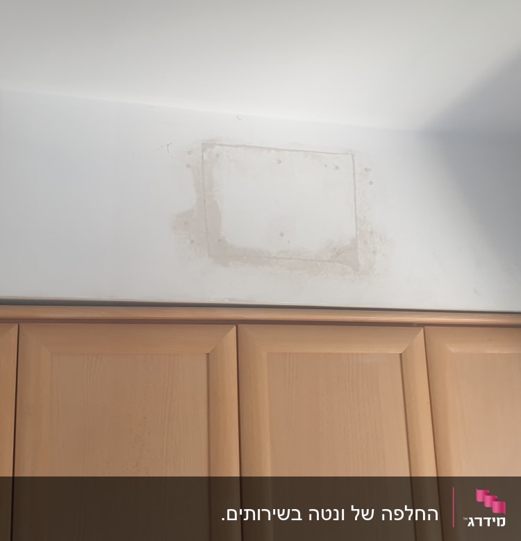 קיר עם סימני תיקון חשמל ליד ארון עץ